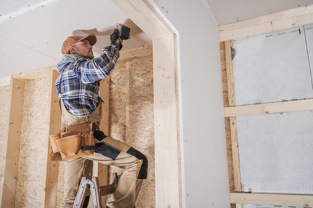 a general contractor on a ladder using a drill on the ceiling